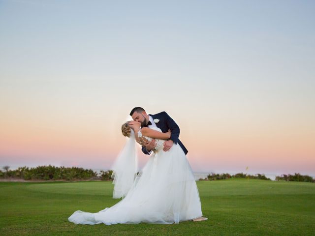 A couple kissing at sunset, with the groom in a dark suit and the bride in a white gown and veil, on a grassy field.