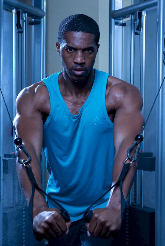 A person working out on a cable machine in a gym, wearing a blue tank top, surrounded by a misty atmosphere.