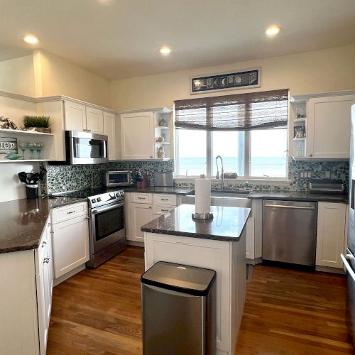 A modern kitchen with white cabinets, stainless steel appliances, an island, and a large window with a view.