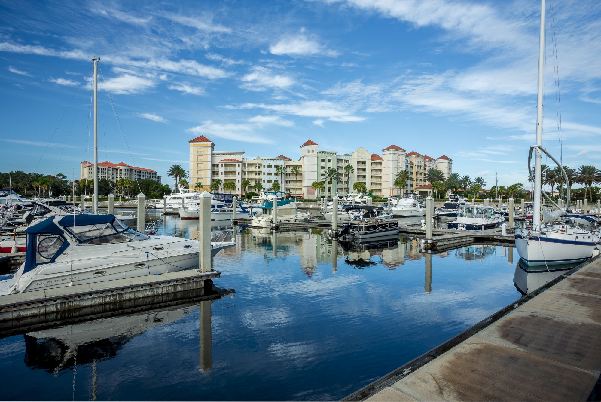 A marina with boats docked along piers and colorful buildings in the background under a clear blue sky.