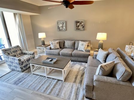 A modern living room with gray sofas, a patterned armchair, coffee table, lamps, and decorative pillows, set on a striped rug.