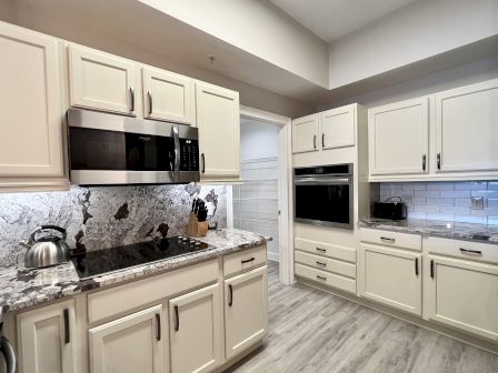 A modern kitchen with cream cabinets, stainless steel appliances, granite countertops, and a tile backsplash, featuring a kettle and knife set.