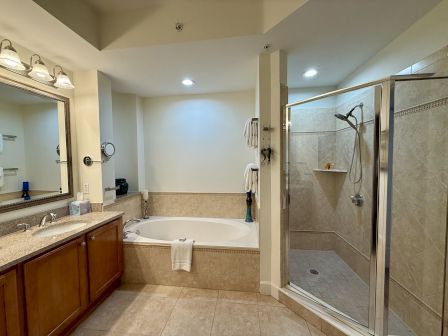 A bathroom with a bathtub, glass shower, vanity with a sink and mirror, and neatly arranged towels and toiletries.