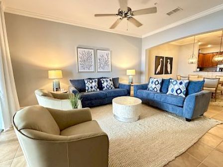A cozy living room with blue sofas, a tan armchair, a round coffee table, and decorative wall art on a light gray wall, under soft lighting.