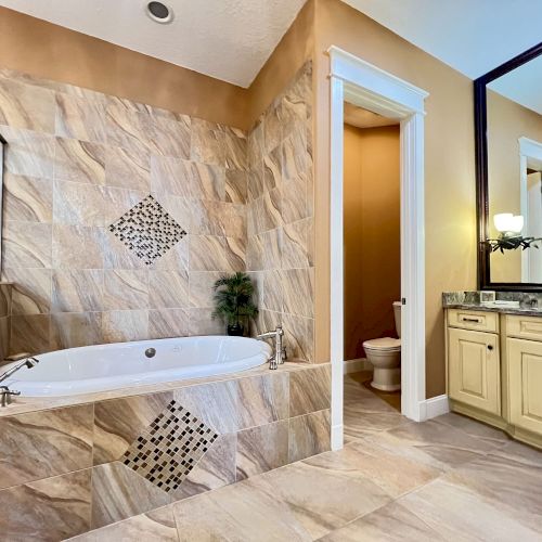 A bathroom with a bathtub, stone tiles, a vanity with a mirror, and a toilet is visible.