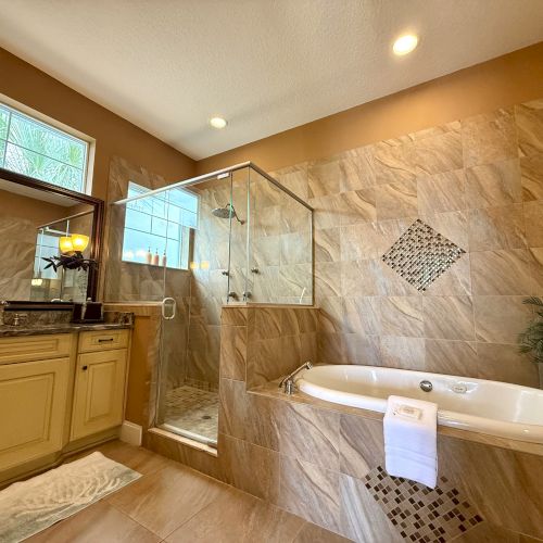 A bathroom featuring a glass-enclosed shower, a bathtub with tile accents, and a vanity with a mirror and lighting on top of it.