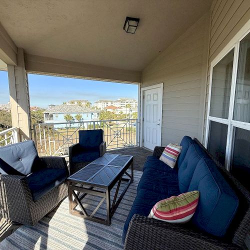A covered patio with wicker furniture, including a couch, chairs, and a table, overlooks a scenic view of buildings and trees.