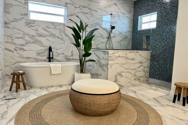 A modern bathroom with a freestanding tub, a plant, mosaic-tiled shower, and round rug, creating a stylish, serene atmosphere.